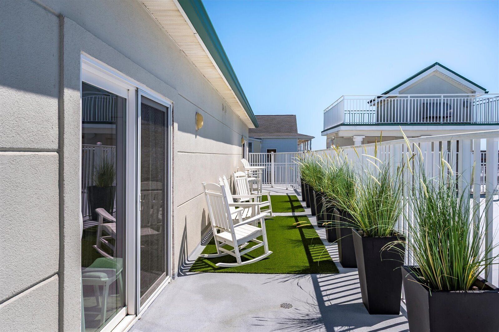 Une terrasse avec des chaises blanches, une petite pelouse et des plantes en pot.