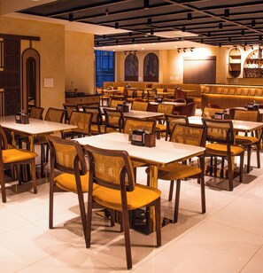 A restaurant interior with multiple tables and chairs, a ceiling with exposed beams, and a wall with a mural. - Snap Inn Rooms By The Buzz House (Anekal)