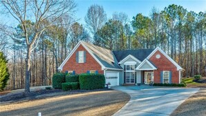 A two-story brick house with a front garage, surrounded by a well-maintained lawn and trees. - Buford Home NEAR everything! (Buford)
