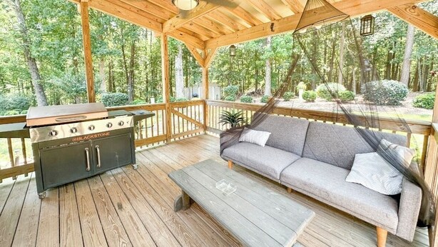 A covered outdoor deck with a grill, a sofa, and a wooden bench. - Buford Home NEAR everything! (Buford)