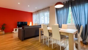Una sala moderna con una pared de acento roja, un televisor de pantalla plana, un sofá, una mesa de comedor con sillas y un ventanal con cortinas.