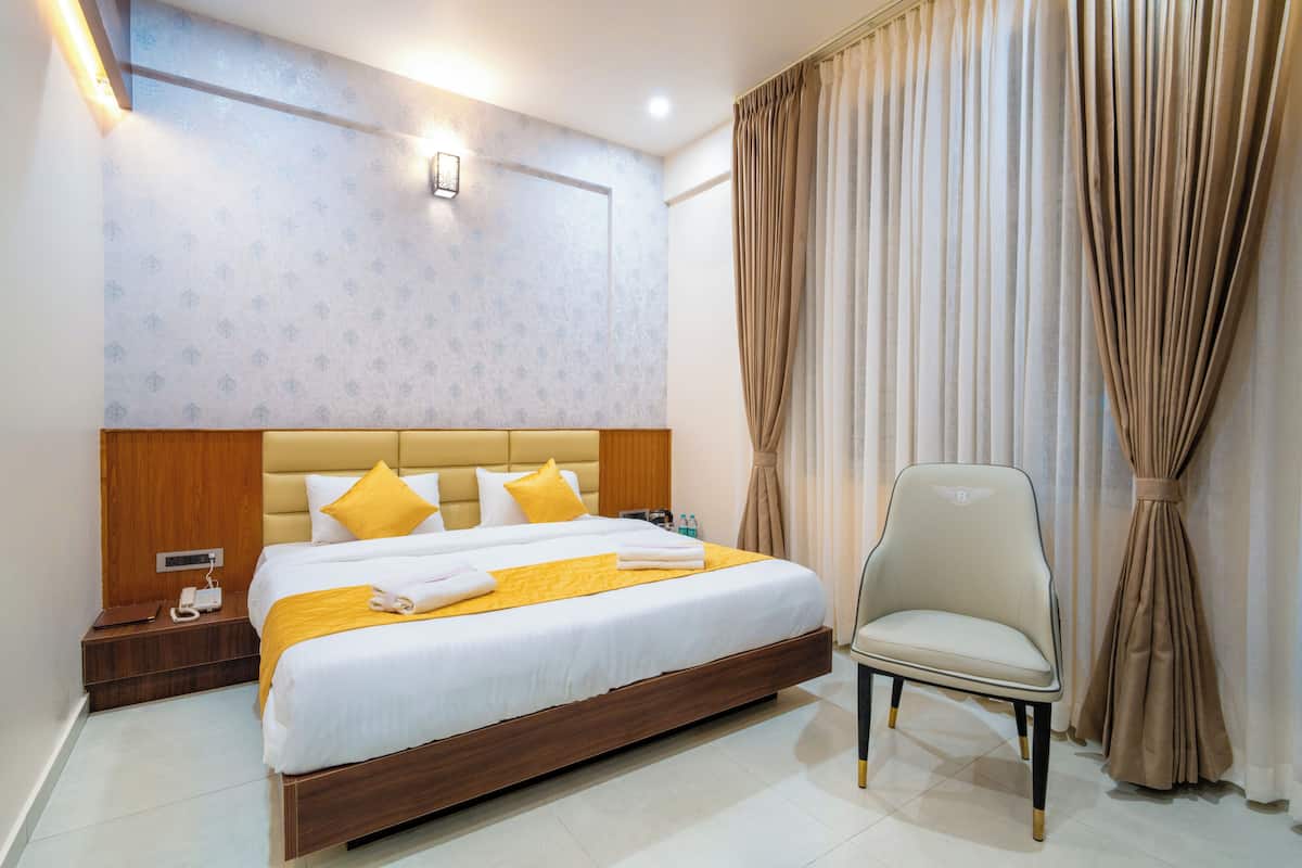 A hotel room with a large bed, a nightstand, a chair, and a wall-mounted light.