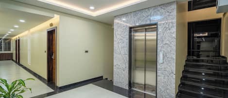 Egy modern szállodakorridor márványfalakkal, lifttel és lépcsőházzal.