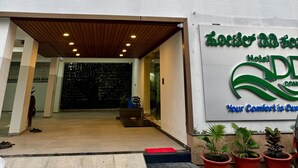 L’entrée d’un hôtel, avec un espace de stationnement couvert, un panneau indicateur et des plantes en pot.