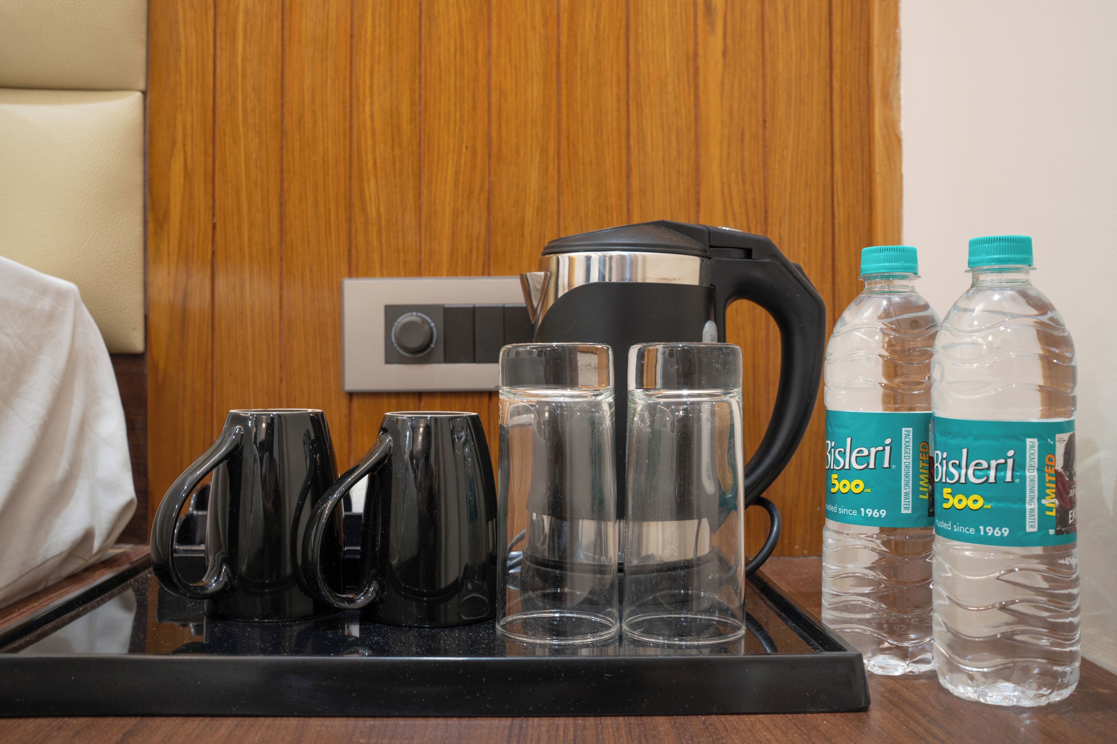 Un plateau avec une bouilloire, quatre tasses et deux bouteilles d’eau Bisleri.