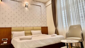 Une chambre d’hôtel avec un grand lit, une table de chevet avec un téléphone, une petite table ronde, une chaise et une fenêtre avec des rideaux.