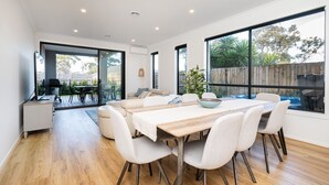 Une salle à manger spacieuse avec une longue table en bois, des chaises blanches et de grandes fenêtres donnant sur le jardin.