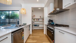 Une cuisine moderne avec des meubles blancs, un lave-vaisselle en acier inoxydable, une cuisinière à gaz et un four encastré.
