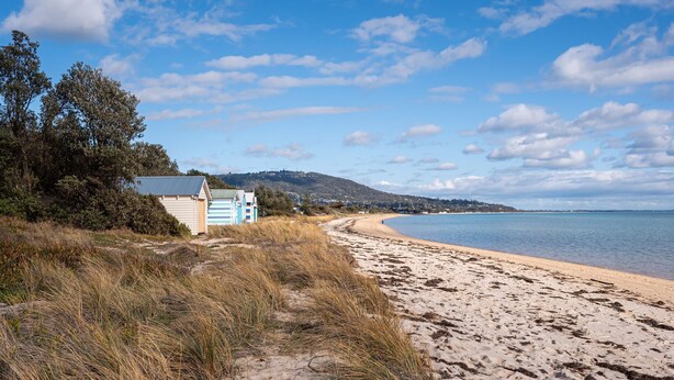 Une plage bordée d’une rangée de cabanes de plage et d’un rivage sablonneux.