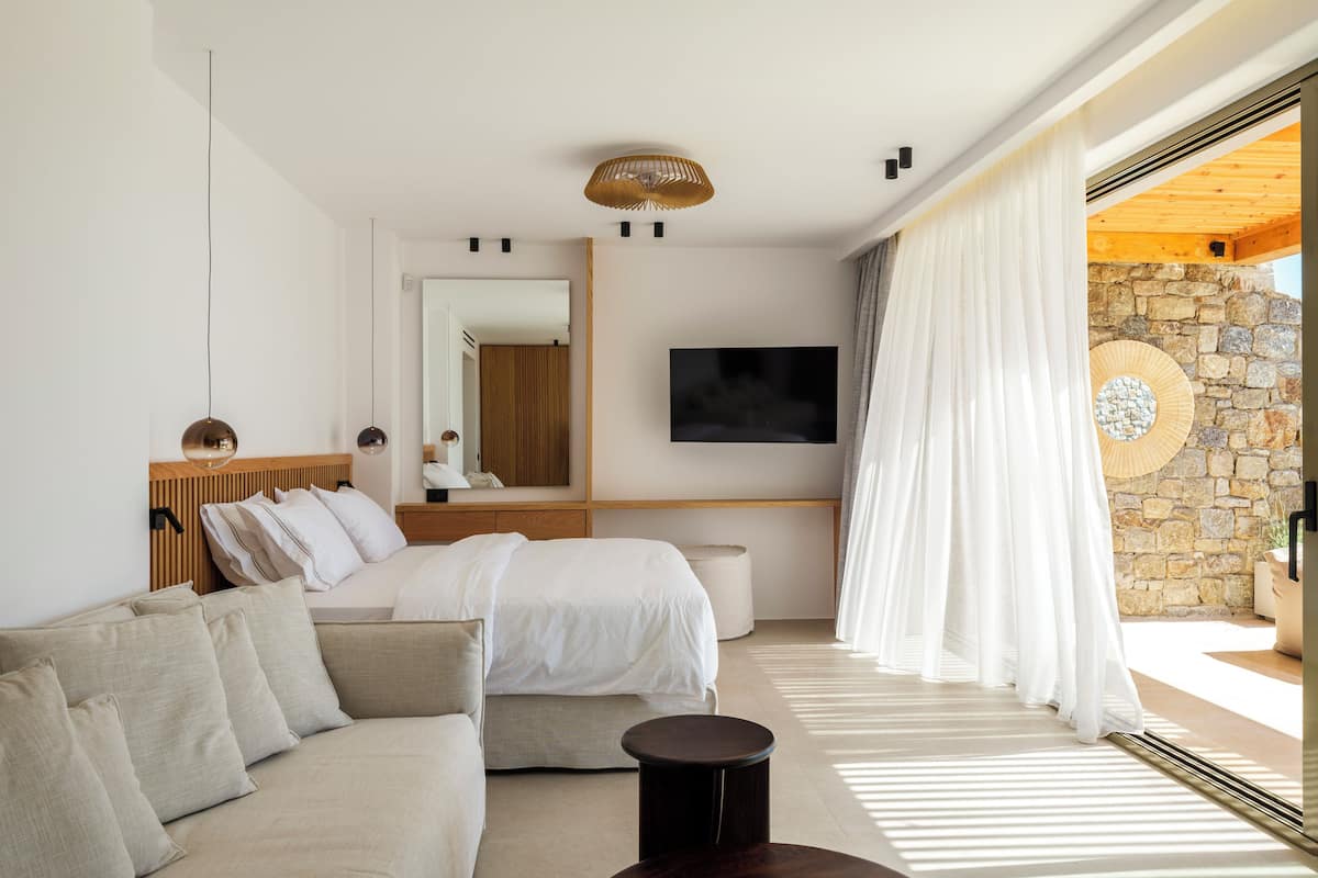 A modern bedroom with a bed, a sofa, a TV, and a stone wall.