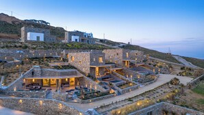 A hillside property with stone buildings, outdoor seating, and a swimming pool. - Panormos Bay Collection (Mykonos)