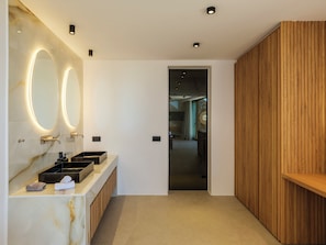 Une salle de bain moderne avec un meuble-lavabo en marbre, deux vasques, un grand miroir avec éclairage intégré et un mur revêtu de panneaux en bois.