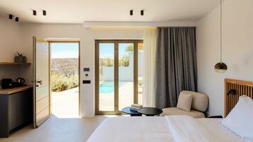 A modern hotel room with a bed, a desk, a chair, a small table, and a view of an outdoor pool and garden.