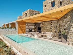 A poolside area with outdoor seating, stone walls, and a modern architectural design. - Panormos Bay Collection (Mykonos)