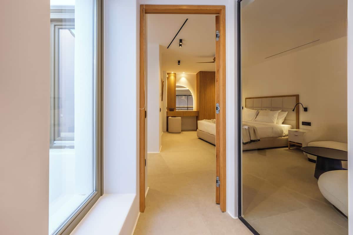 A hotel room with a bed, bedside table, and a view through an open door.