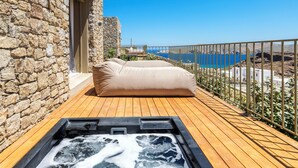 A wooden deck with a hot tub, a stone wall, and a view of the sea. - Panormos Bay Collection (Mykonos)