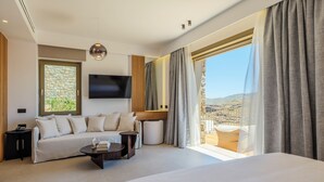 A modern hotel room with a large bed, a sofa, a TV, and a balcony with a view. - Panormos Bay Collection (Mykonos)