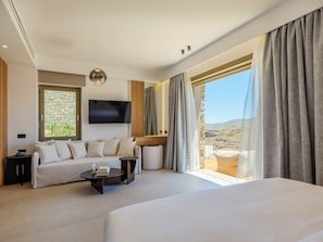A modern hotel room with a large bed, a sofa, a TV, and a balcony with a view. - Panormos Bay Collection (Mykonos)