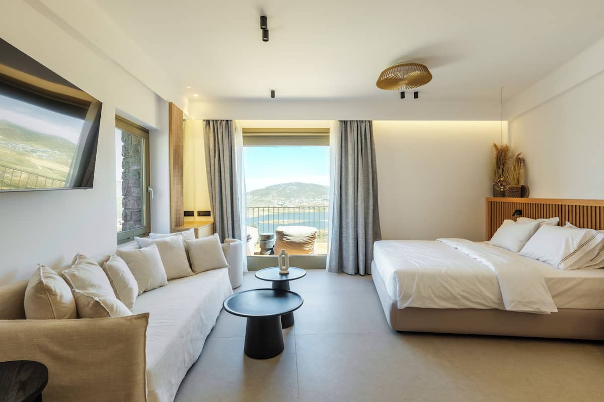 A modern hotel room with a sofa, a bed, a small table, and a view of the outdoors.