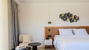 Una habitación de hotel con una cama, una mesita de noche, una silla, una pequeña mesa y una obra de arte en la pared.