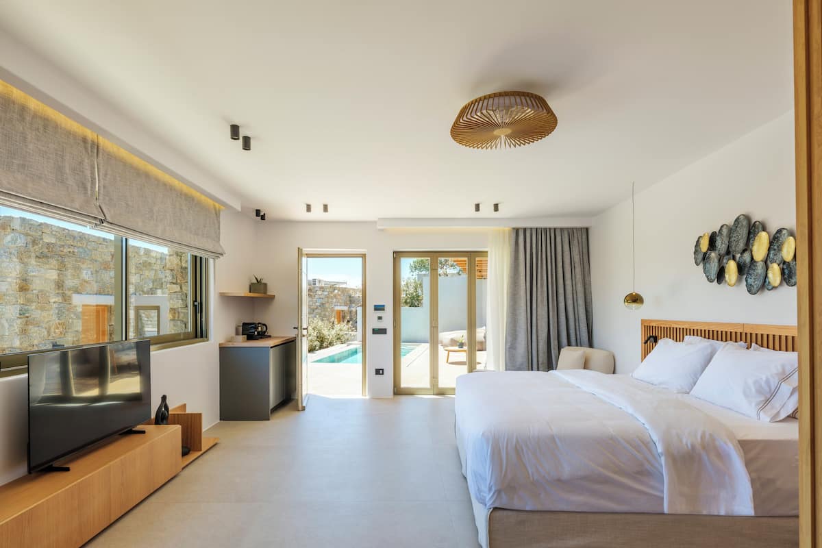 A modern bedroom with a TV, a bed, a small desk, and a view of an outdoor pool.