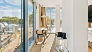 A modern hotel room with a large sliding glass door leading to an outdoor area, a dining table with chairs, a small TV, and a bedside table with a lamp.