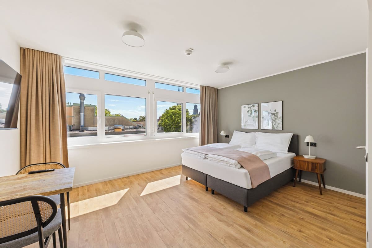 Une chambre d’hôtel moderne avec un grand lit, un bureau et une fenêtre donnant sur la ville.