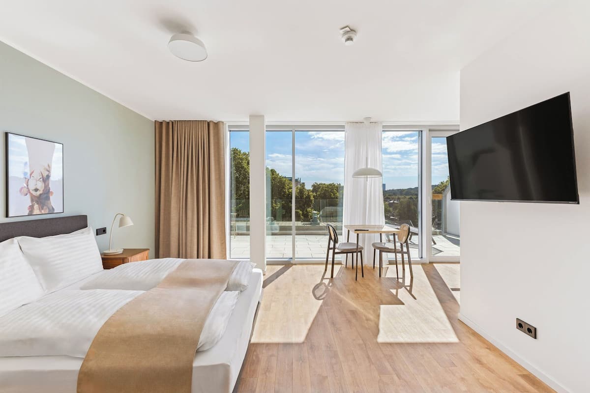 Une chambre d’hôtel moderne équipée d’un lit, d’une télévision, d’un coin repas et d’un balcon avec vue.