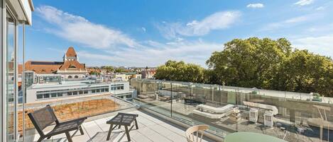 A rooftop terrace with outdoor seating, a view of a historic building, and a glass barrier.
