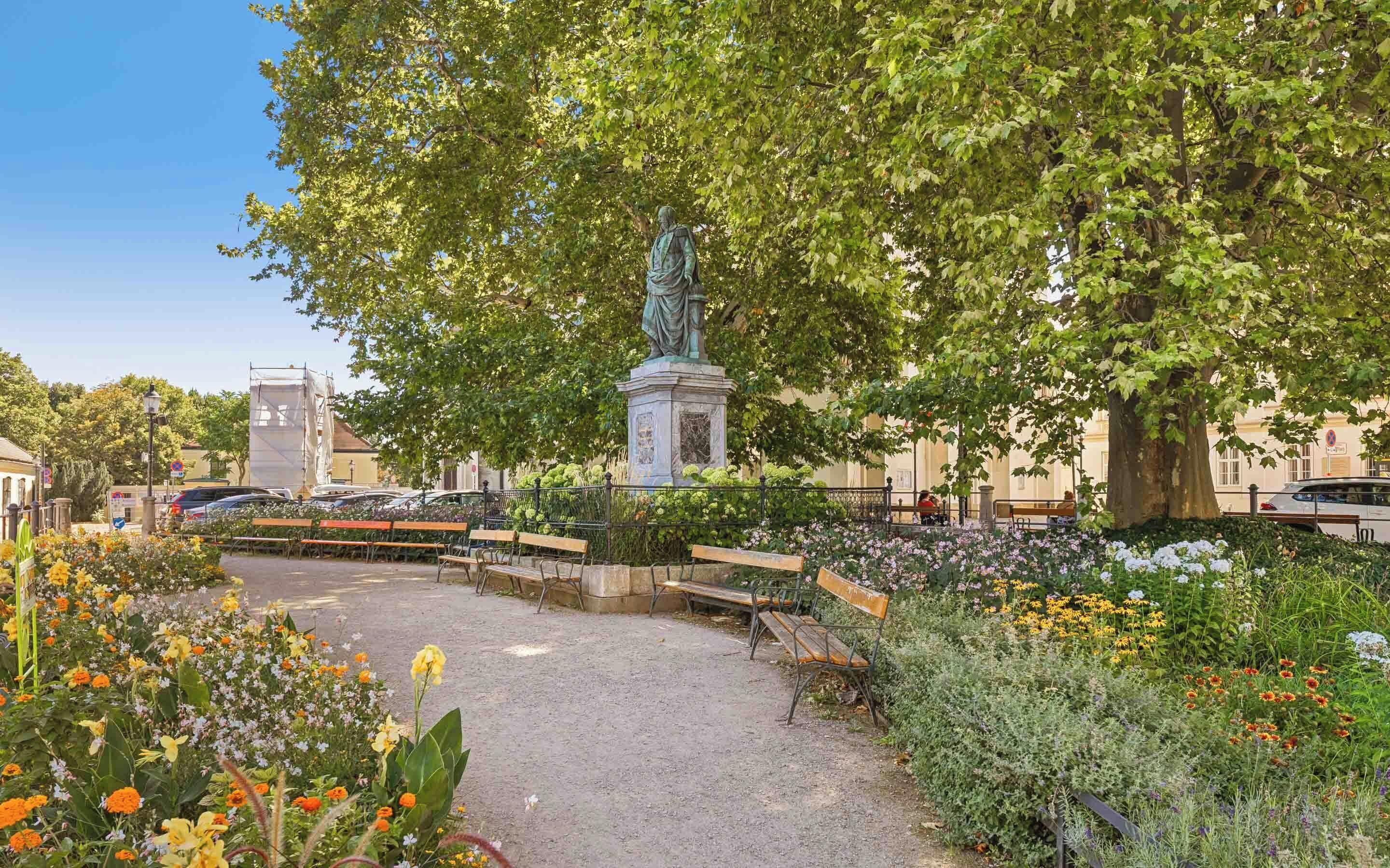 A park with benches, a statue, and flower beds.