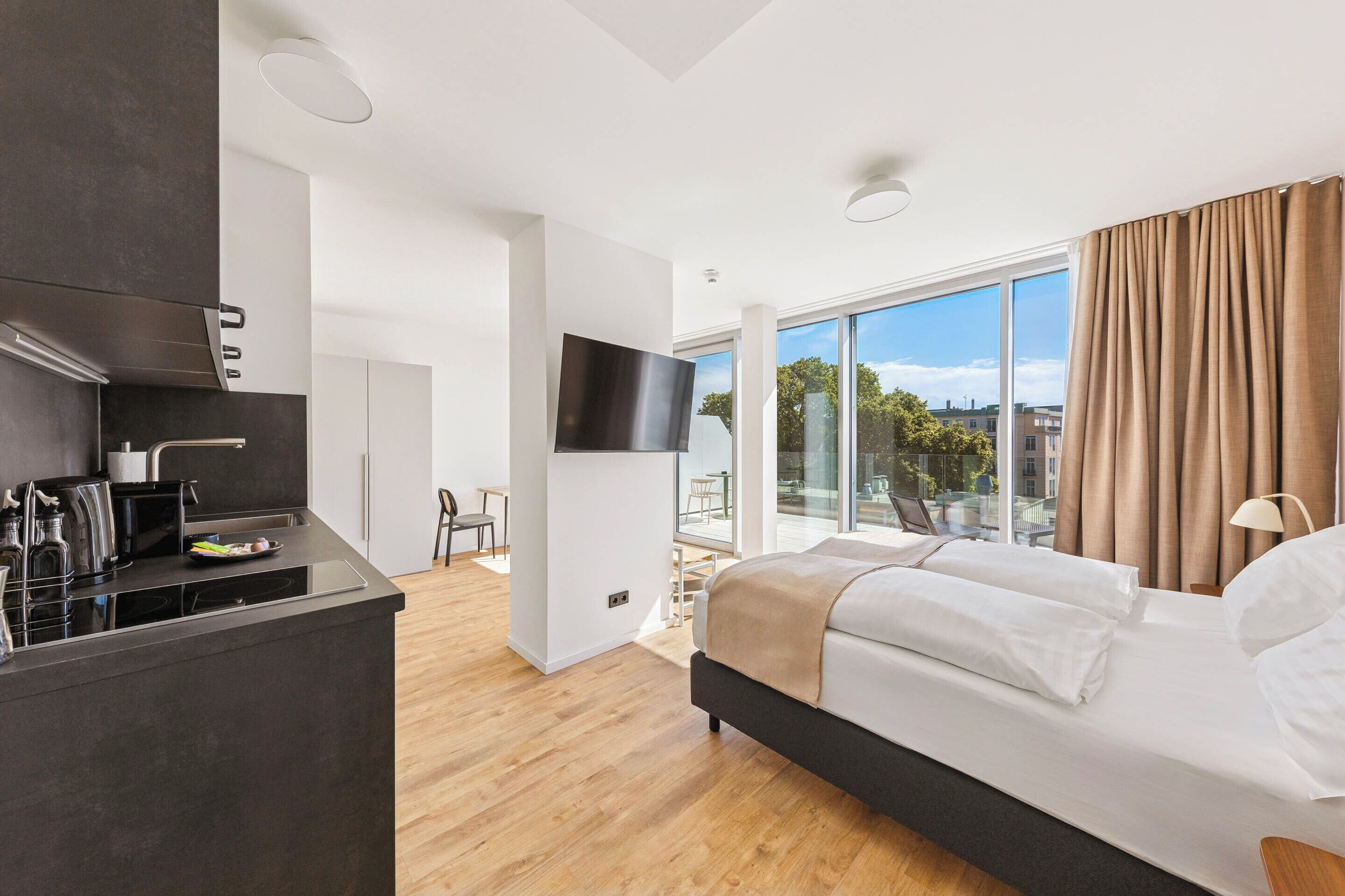 Ein modernes Hotelzimmer mit einem großen Bett, einer Küchenzeile und einem Balkon mit Blick.