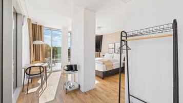 A modern hotel room with a bed, a desk with a chair, a small table with a tray, and a balcony with a view.