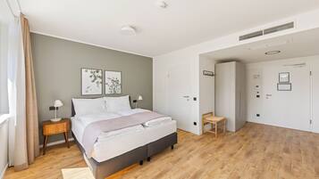 A modern bedroom with a large bed, bedside tables, a chair, and a door leading to another room.