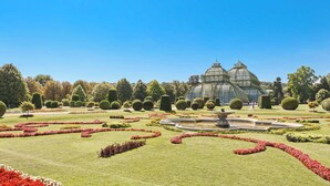 A formal garden with a central fountain, manicured lawns, and a large greenhouse structure.