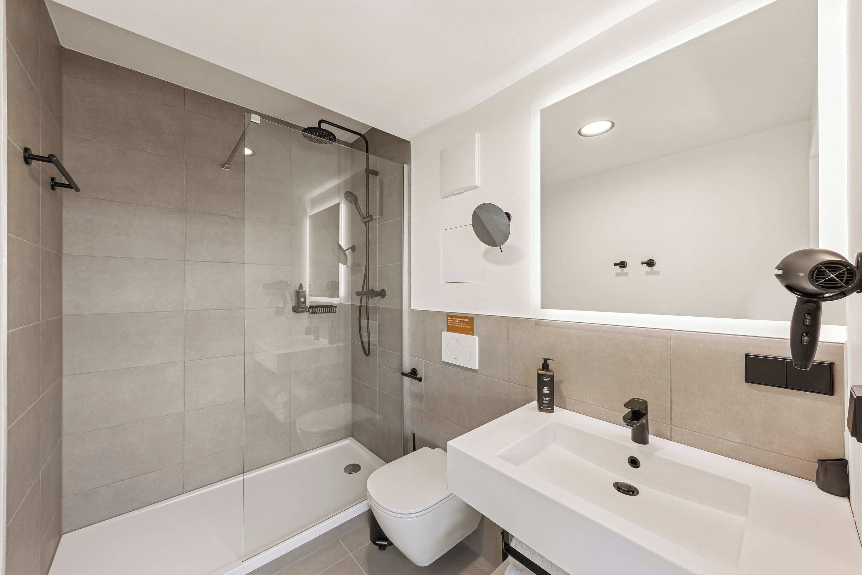 Un baño moderno con ducha de vidrio, inodoro blanco y lavamanos blanco con espejo arriba.