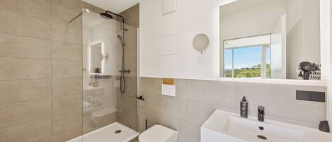 A modern bathroom with a glass-enclosed shower, a white toilet, and a large sink with a mirror above it.