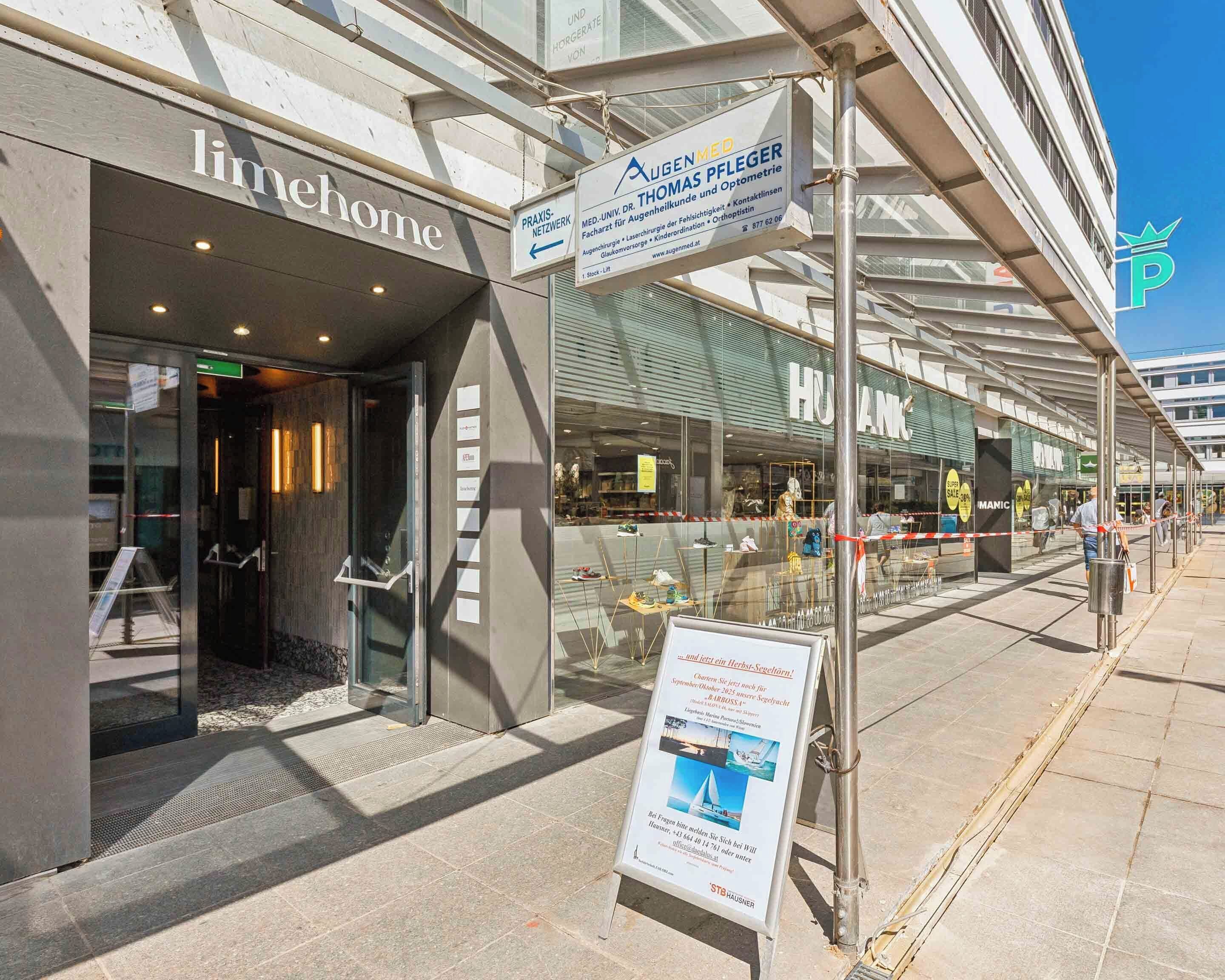 Un edificio moderno con fachada de vidrio, un cartel con la leyenda 'Augenmedeg' que indica una clínica médica, y un cartel de 'HUBANK' que sugiere un banco o institución financiera.