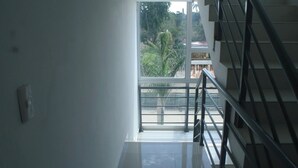 A view from a window to a balcony with a metal railing, a clear sky, and a palm tree in the background.