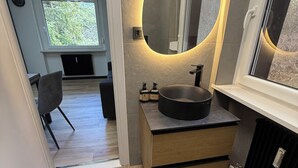 Un baño moderno con un espejo ovalado grande, un lavabo negro y un tocador de madera.