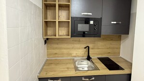 Una cocina compacta con microondas integrado, un lavamanos y armarios de madera.