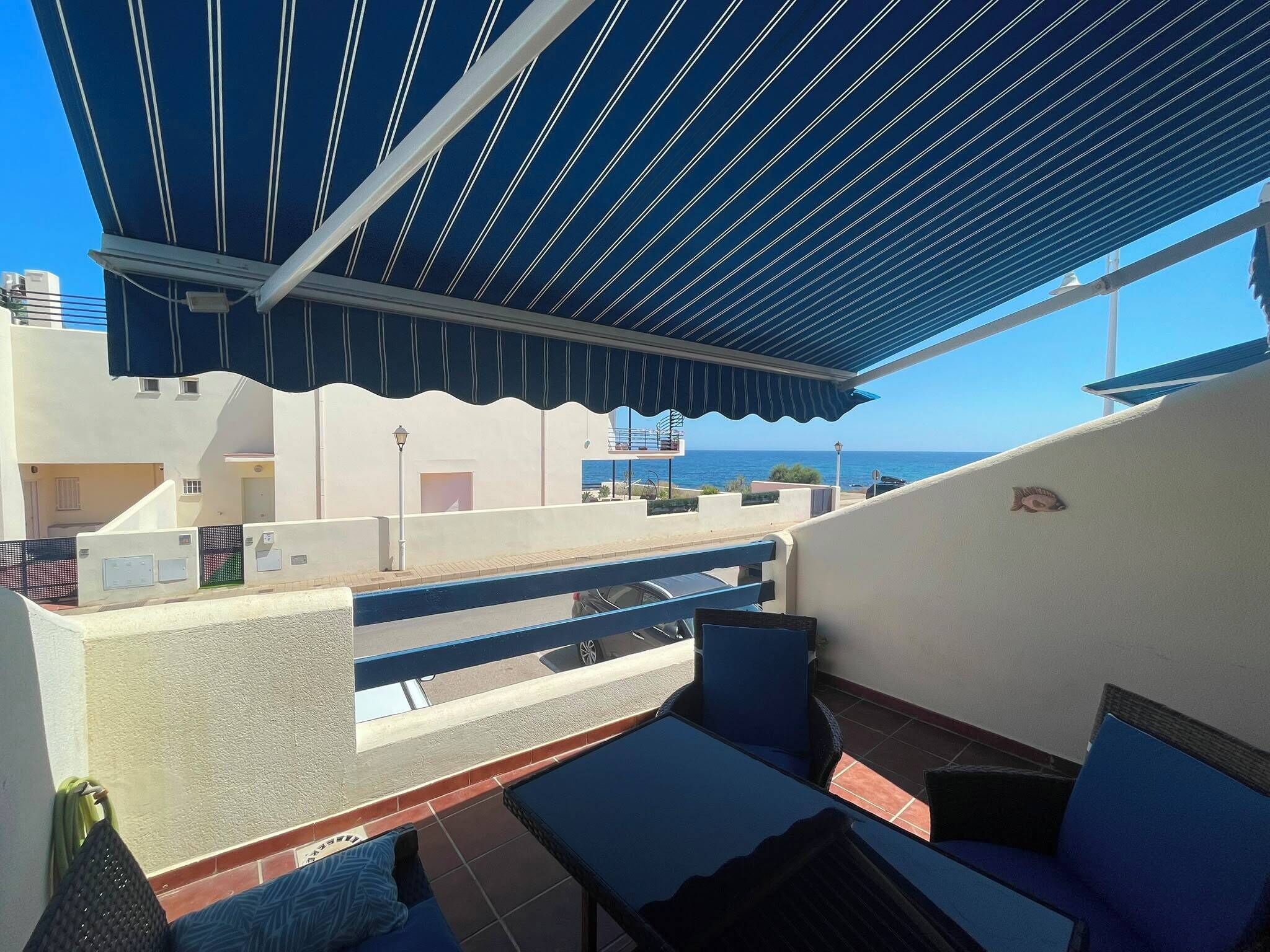 A rooftop terrace with a view of the sea, outdoor seating, and a covered area with a striped awning.