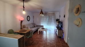 A living room with a sofa, a dining table, and chairs, a TV on a stand, and a hanging light fixture. - Casa Luna ;) ... Semi-detached house just a few steps from the ocean 🌊 (Cuevas del Almanzora)
