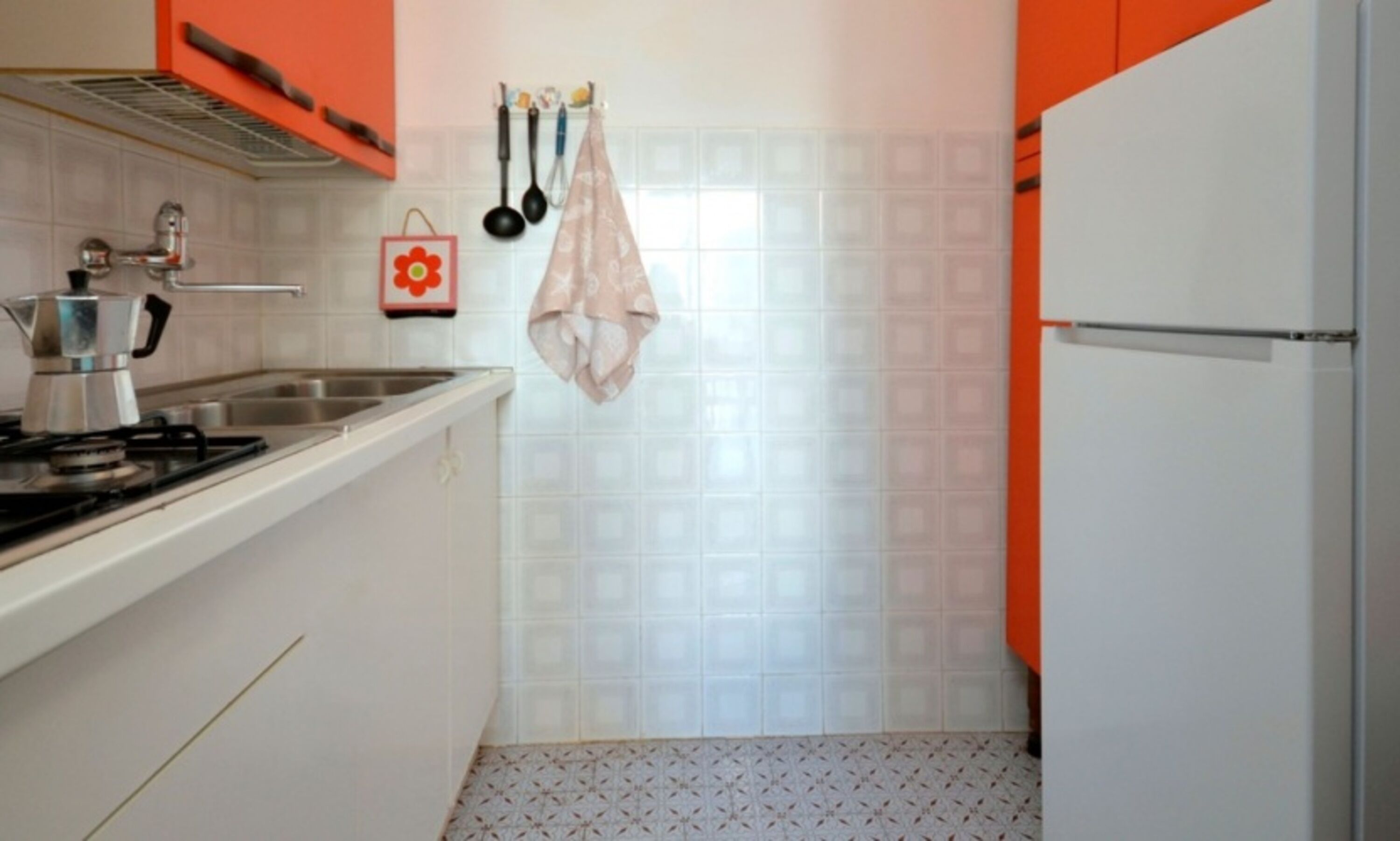 A kitchen with a stove, sink, and hanging utensils.