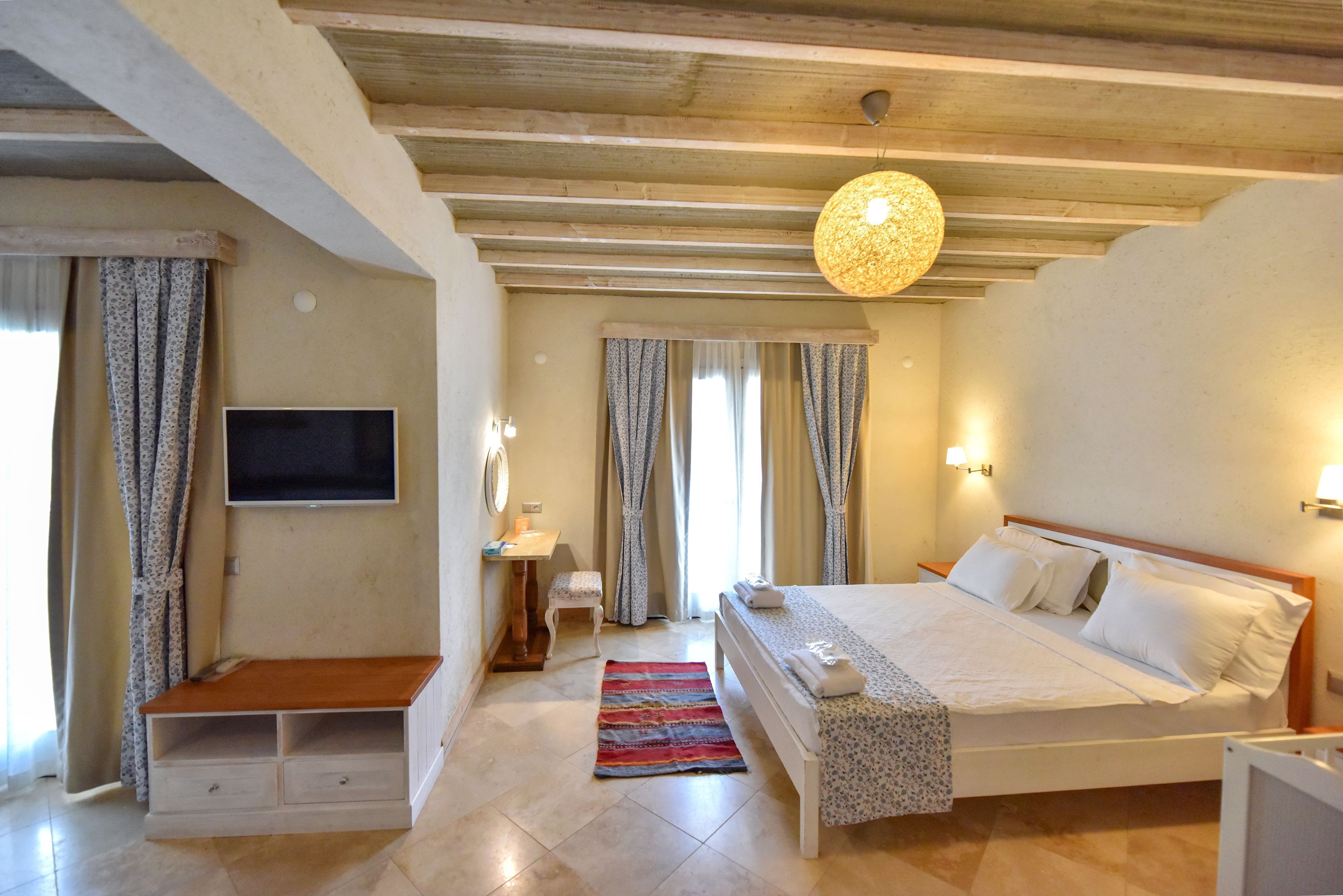 Un dormitorio con cama, televisor, escritorio y ventana con cortinas.