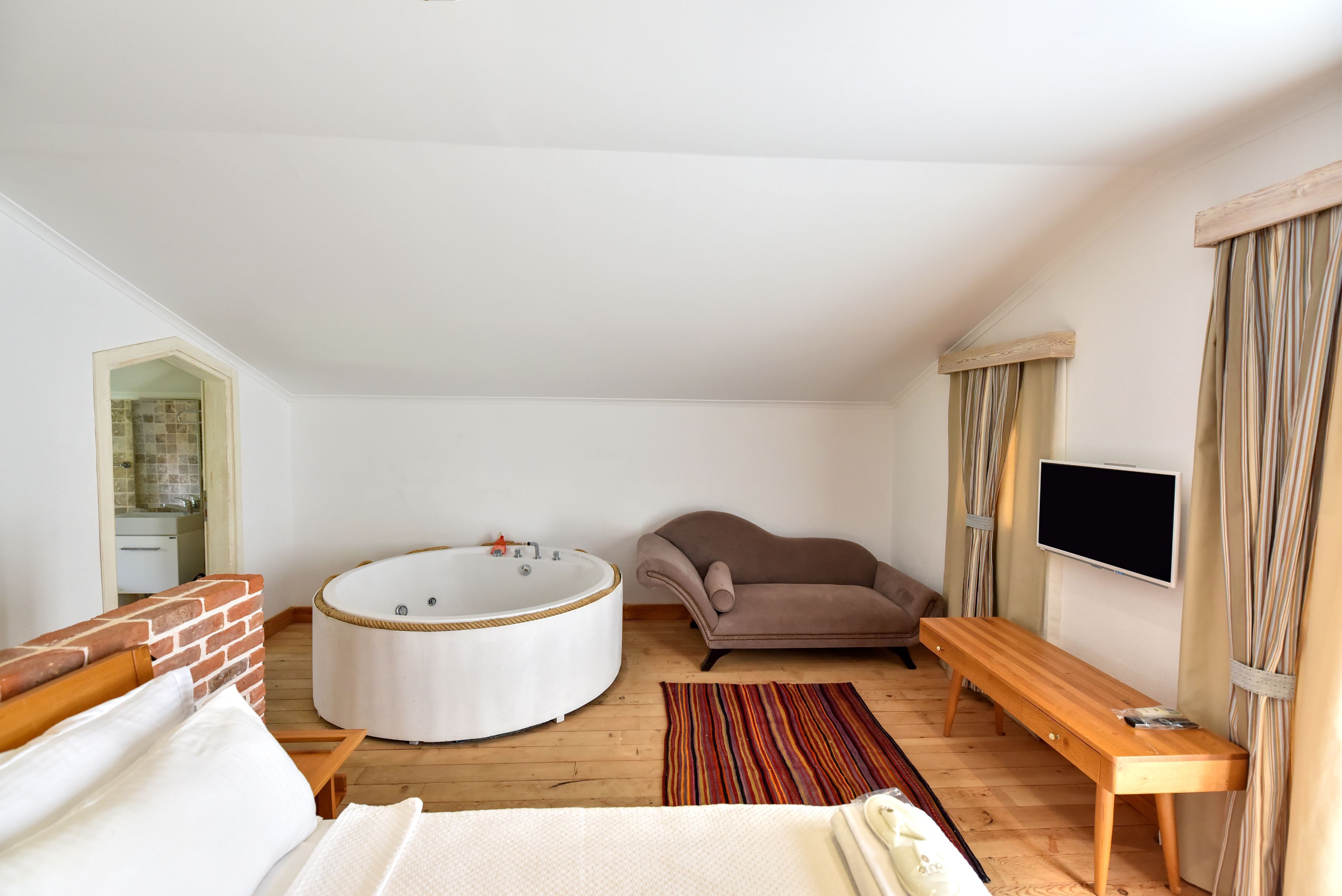 A bedroom with a large round bathtub, a sofa, a wooden bench, a TV, and a small table.