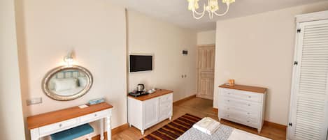 A hotel room with a wooden desk, a mirror, a television, a wardrobe, and a bed with towels.