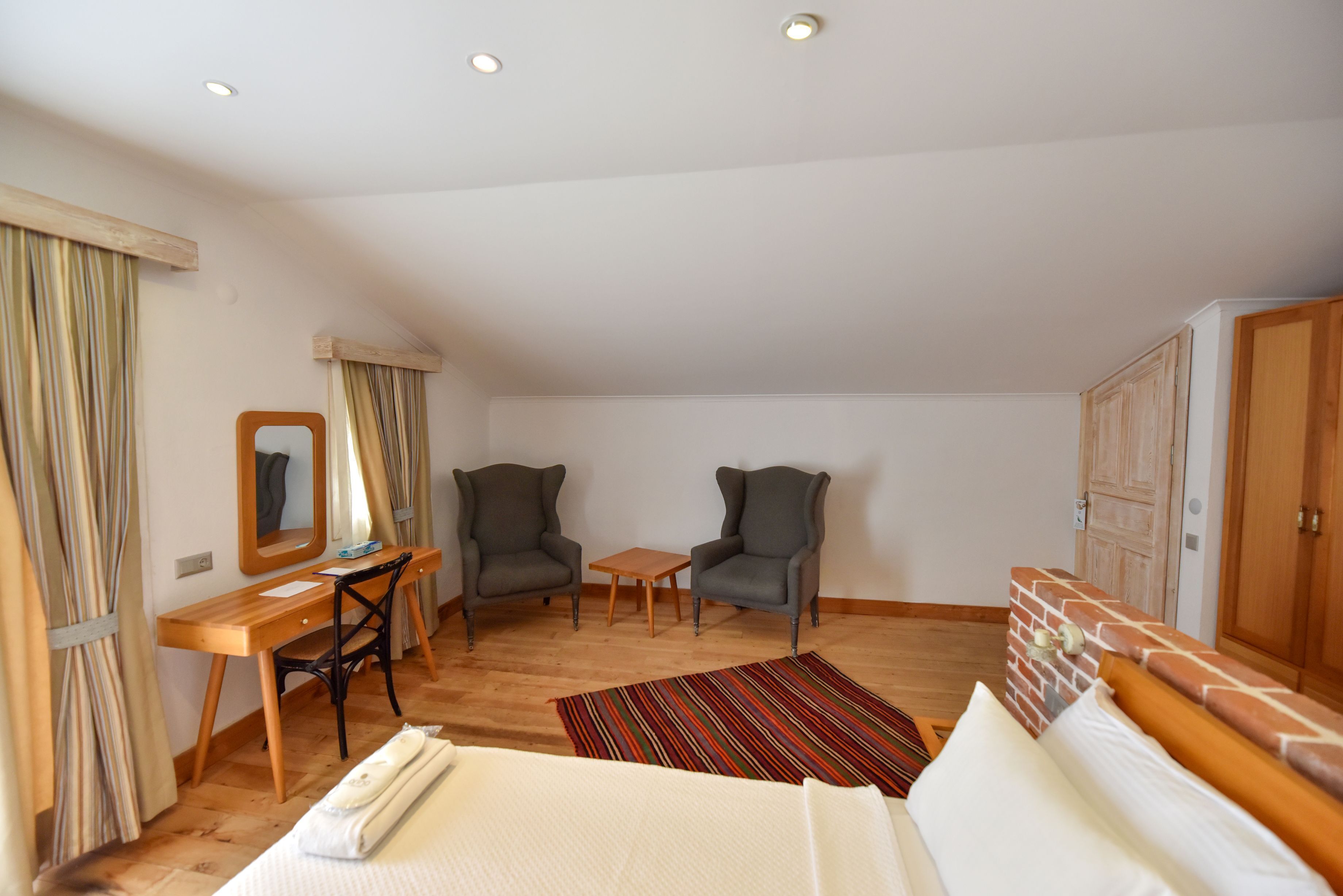 A bedroom with a bed, a desk, two armchairs, a small table, a mirror, and a wardrobe.