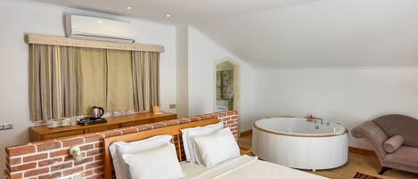 A spacious bedroom with a large bed, a wooden bench, a small table, a round bathtub, and a chair.