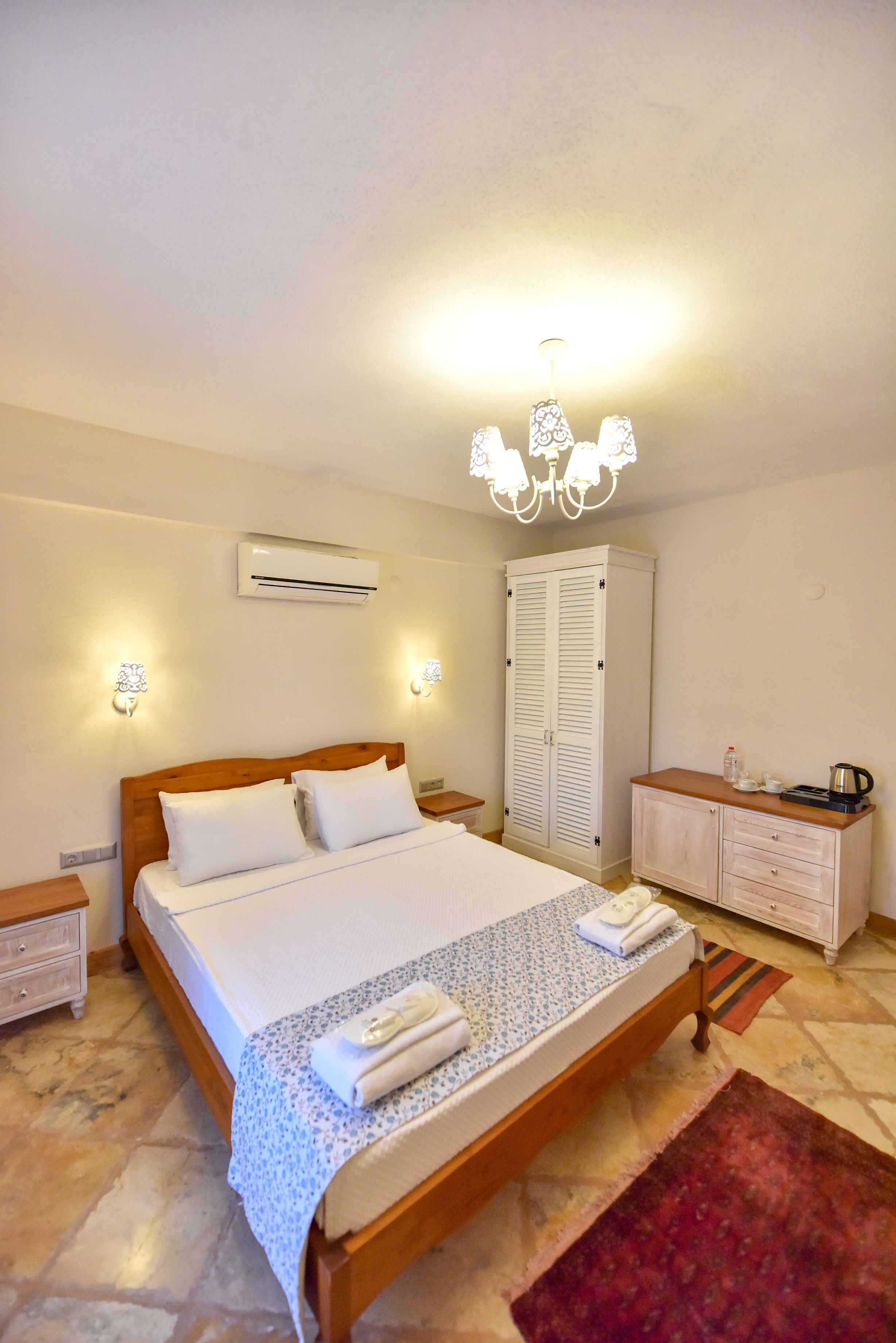 A bedroom with a wooden bed, white linens, a wardrobe, a nightstand, and a chandelier.