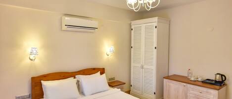 A bedroom with a wooden bed, white linens, a wardrobe, a nightstand, and a chandelier.